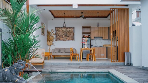 A modern living area with a pool, wooden furniture, and a kitchen visible through an open door.