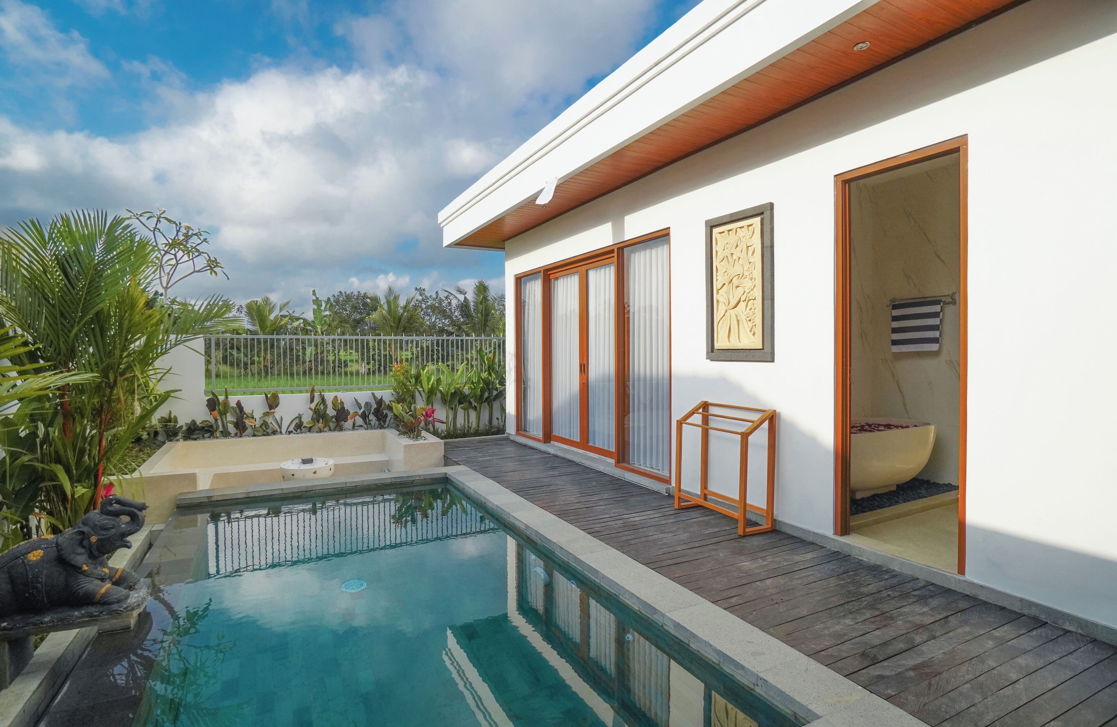 A modern house with a swimming pool, wooden deck, and a large sliding glass door leading to a bathroom with a bathtub.