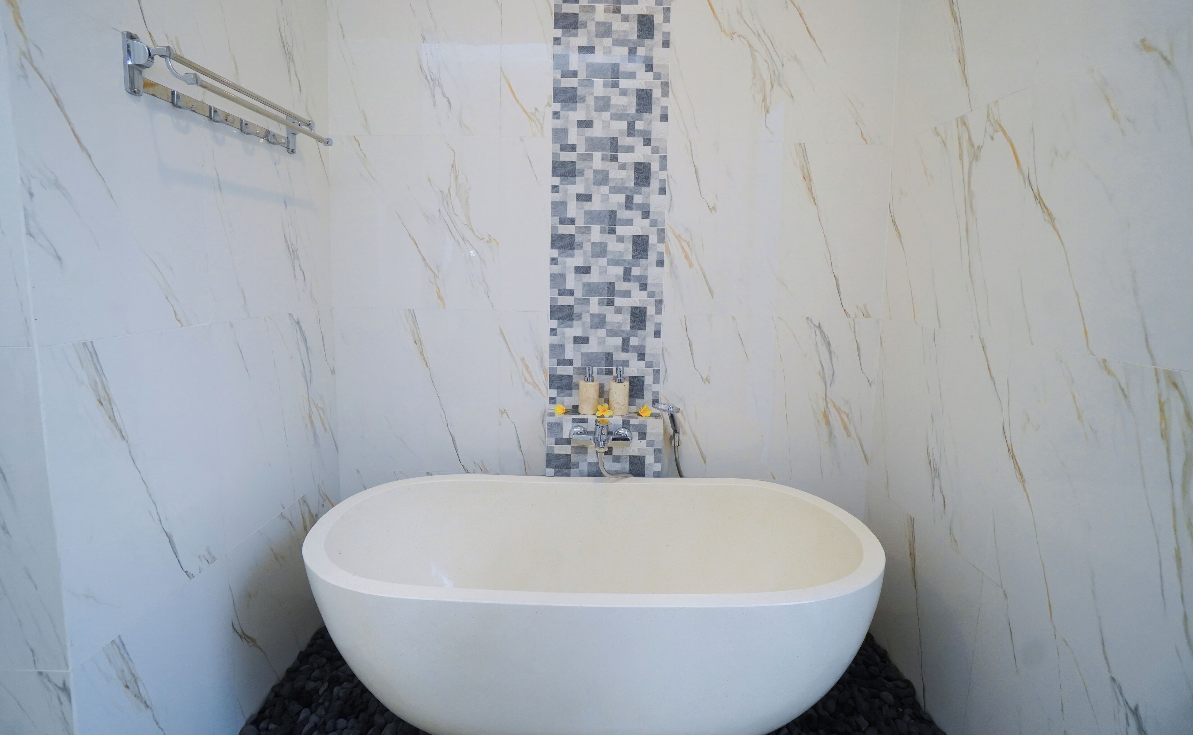 A bathroom with a freestanding bathtub, a towel rack, and a tiled shower wall.
