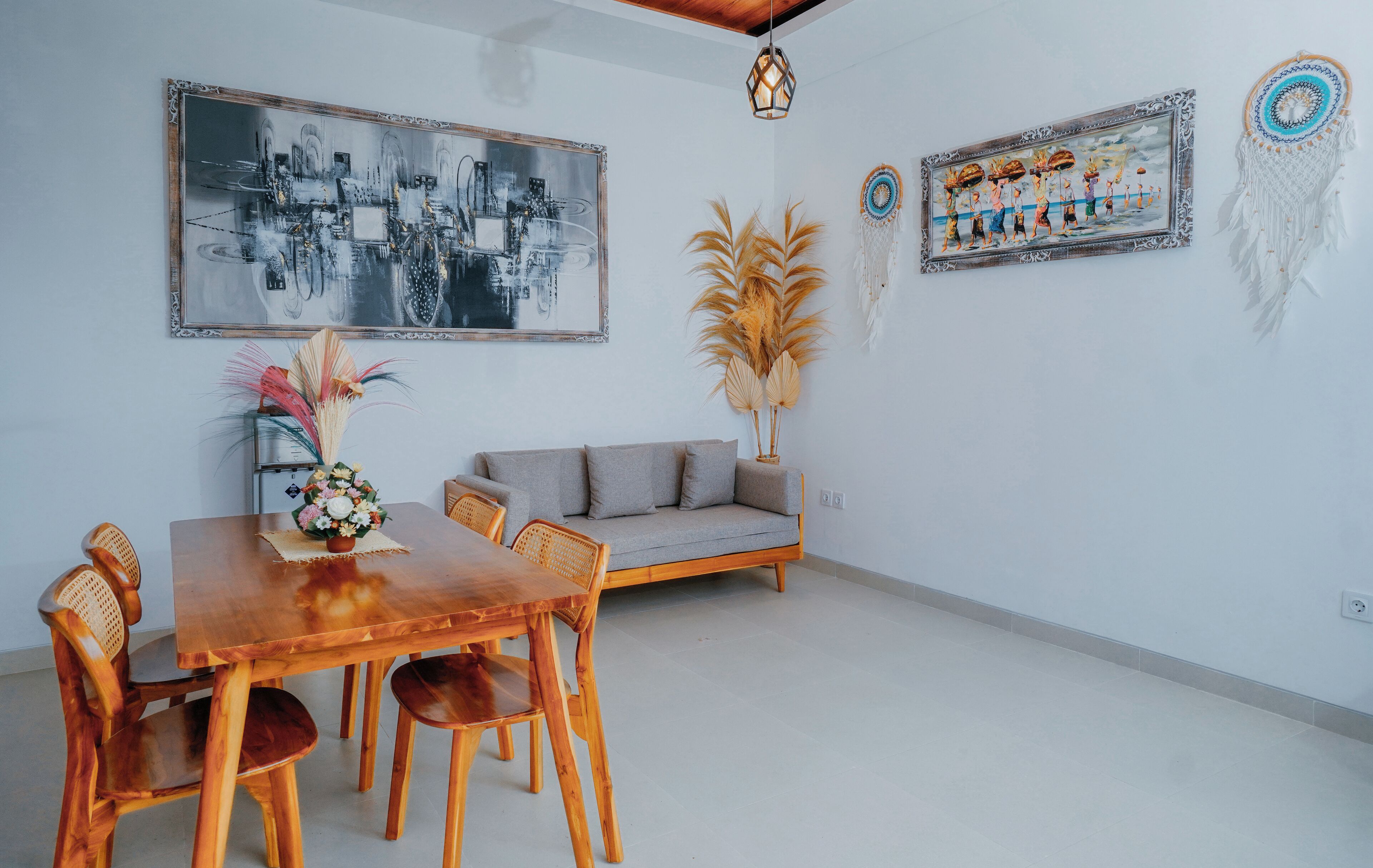 A dining area with a wooden table and chairs, a sofa, and two framed artworks on the wall.