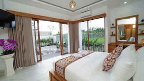 A bedroom with a large bed, a TV, and a sliding glass door leading to a balcony with plants.