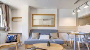 Ein modernes Zimmer mit einer Couch, einem kleinen Tisch, einem Esstisch mit Stühlen und einem Spiegel an der Wand.