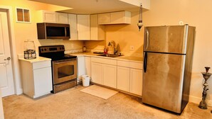 A compact kitchen with white cabinets, a stainless steel refrigerator, a microwave, an oven, and a sink. - Charming 2-bedroom Basement Apt with WiFi, AC in delightful Bryans Road Maryland (Bryans Road)