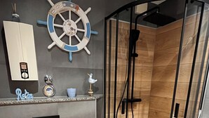 Un baño moderno con suelo de madera, inodoro, lavabo con encimera de madera, decoración de timón de barco y cabina de ducha.