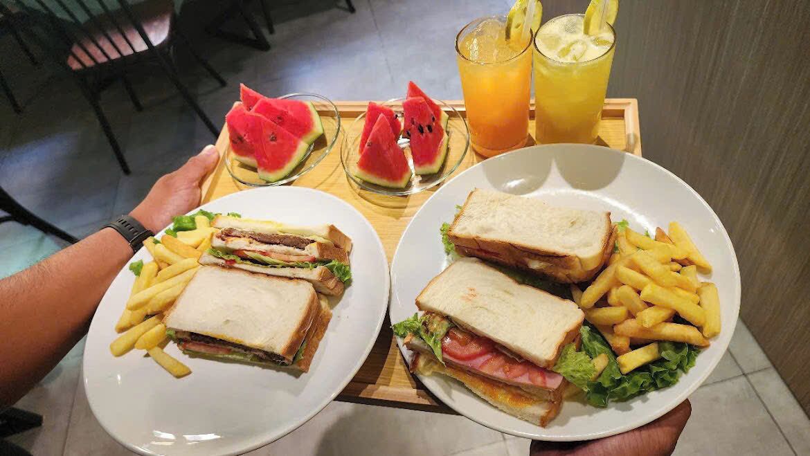 Eine Schale mit zwei Sandwiches und Pommes, ein Glas Orangensaft und Wassermelonenscheiben.
