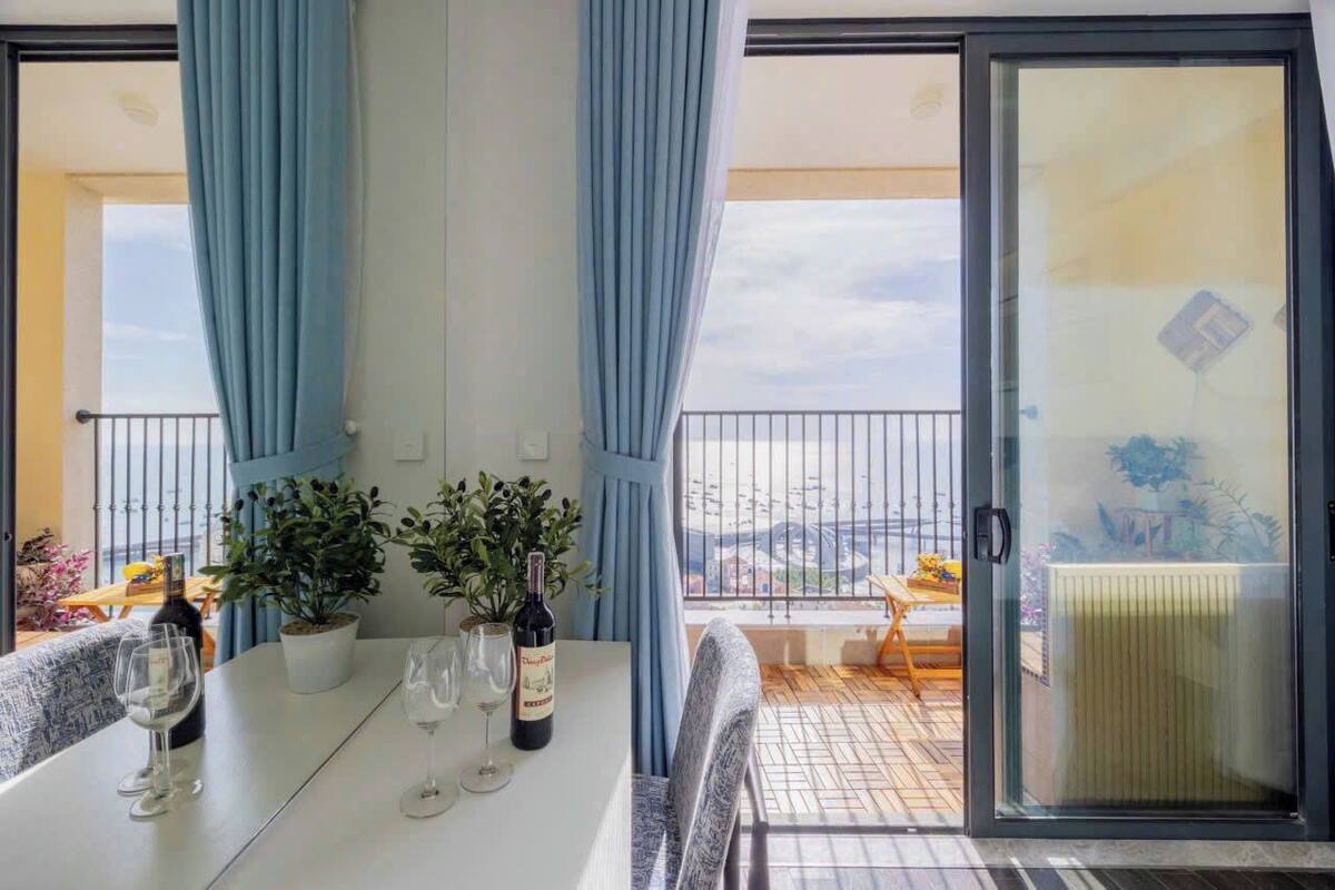 A balcony with a table set for dining, potted plants, and a bottle of wine.
