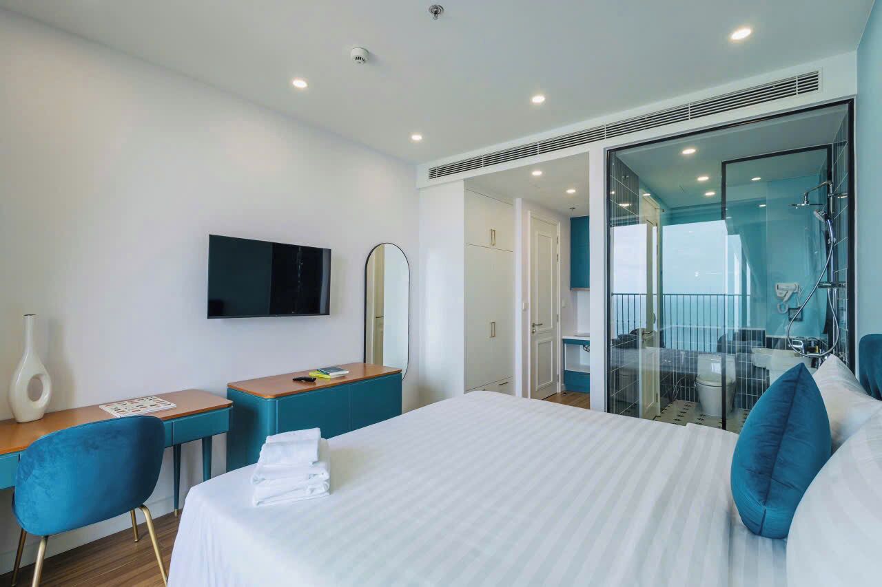 Ein modernes Hotelzimmer mit einem großen Bett, einem Schreibtisch mit Stuhl, einem Flachbildfernseher und einer Duschkabine aus Glas.