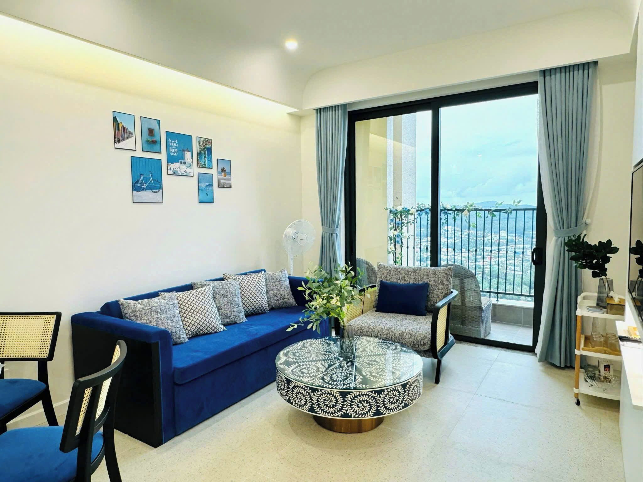 A modern living room with a blue sofa, a round coffee table, and a view of the city through large windows.