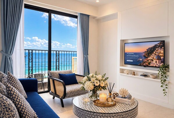 A modern living room with a balcony overlooking a coastal view, a television mounted on the wall, and a round coffee table with decorative items. - Skyline Hillside Apartment Phu Quoc (Phu Quoc)