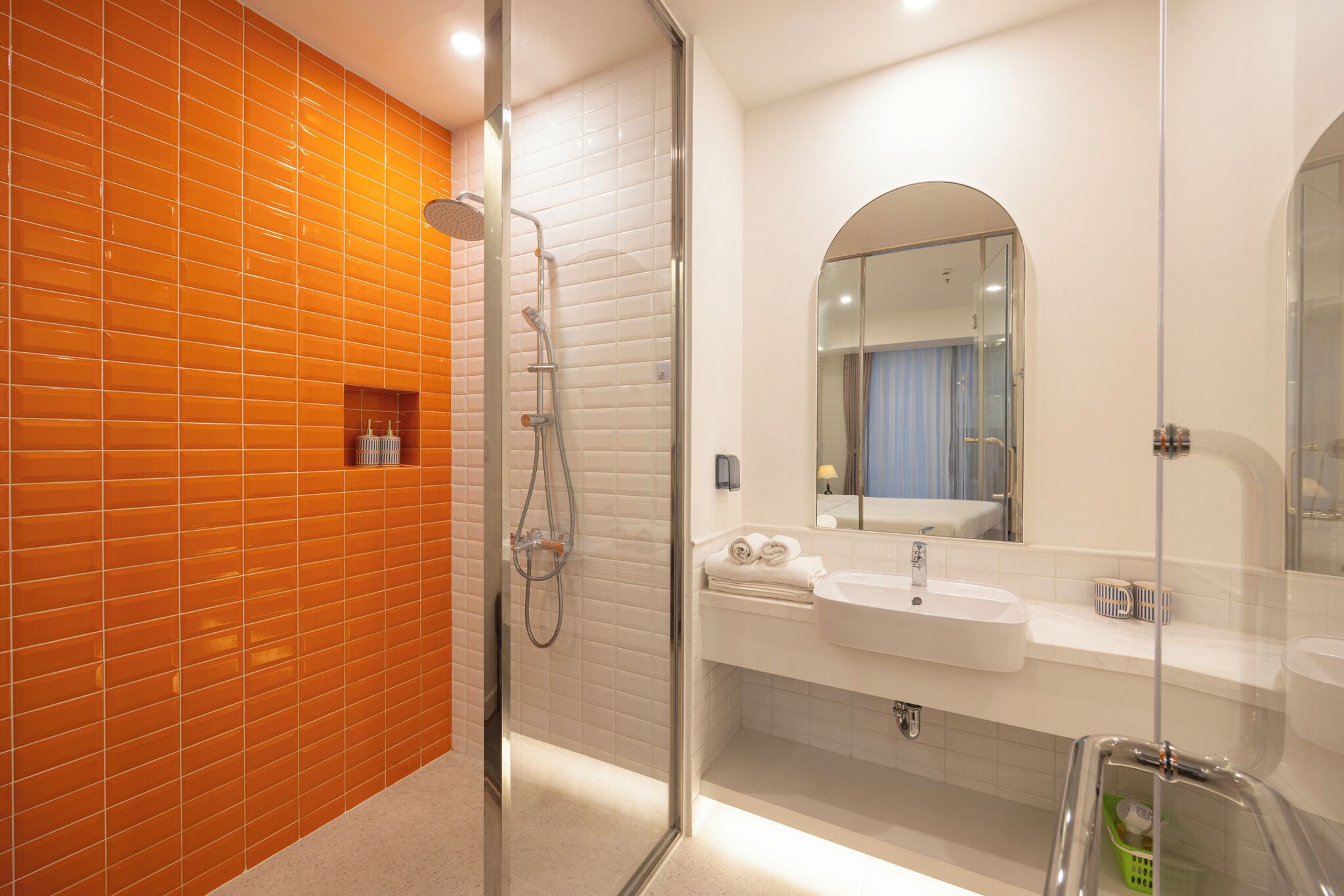 Een moderne badkamer met een douchecabine van glas, een witte wastafel en een spiegel erboven.