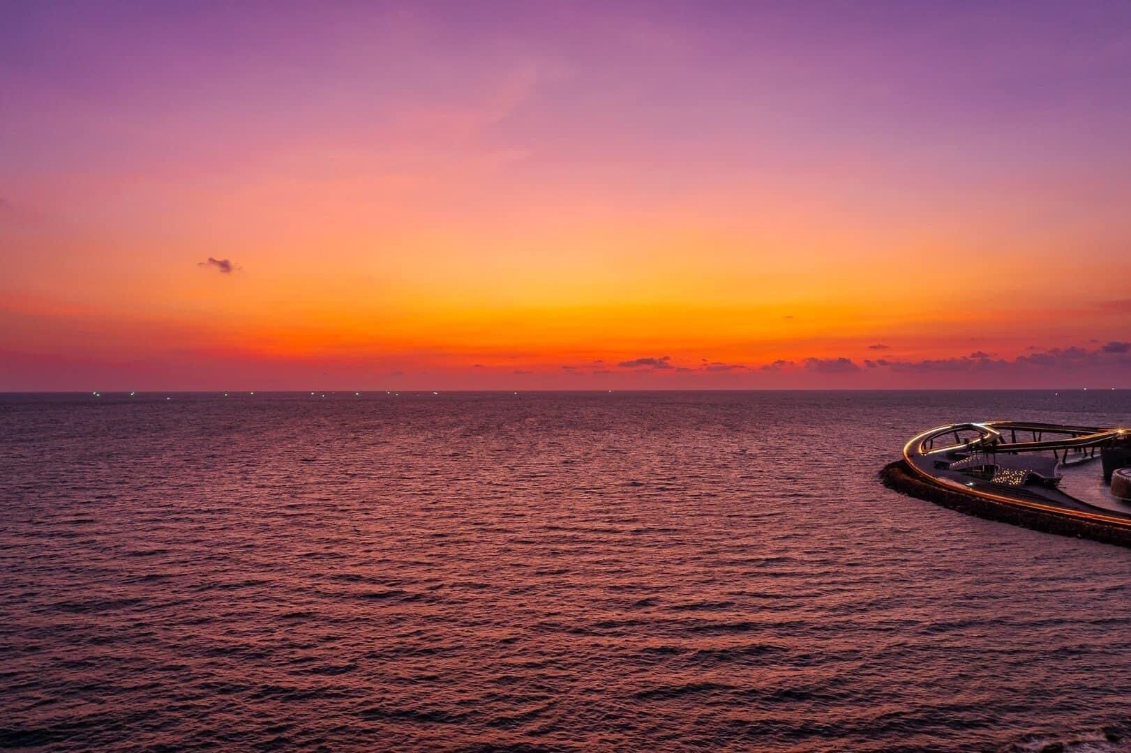Um pôr do sol sobre um mar calmo, com um cais se estendendo para a água.