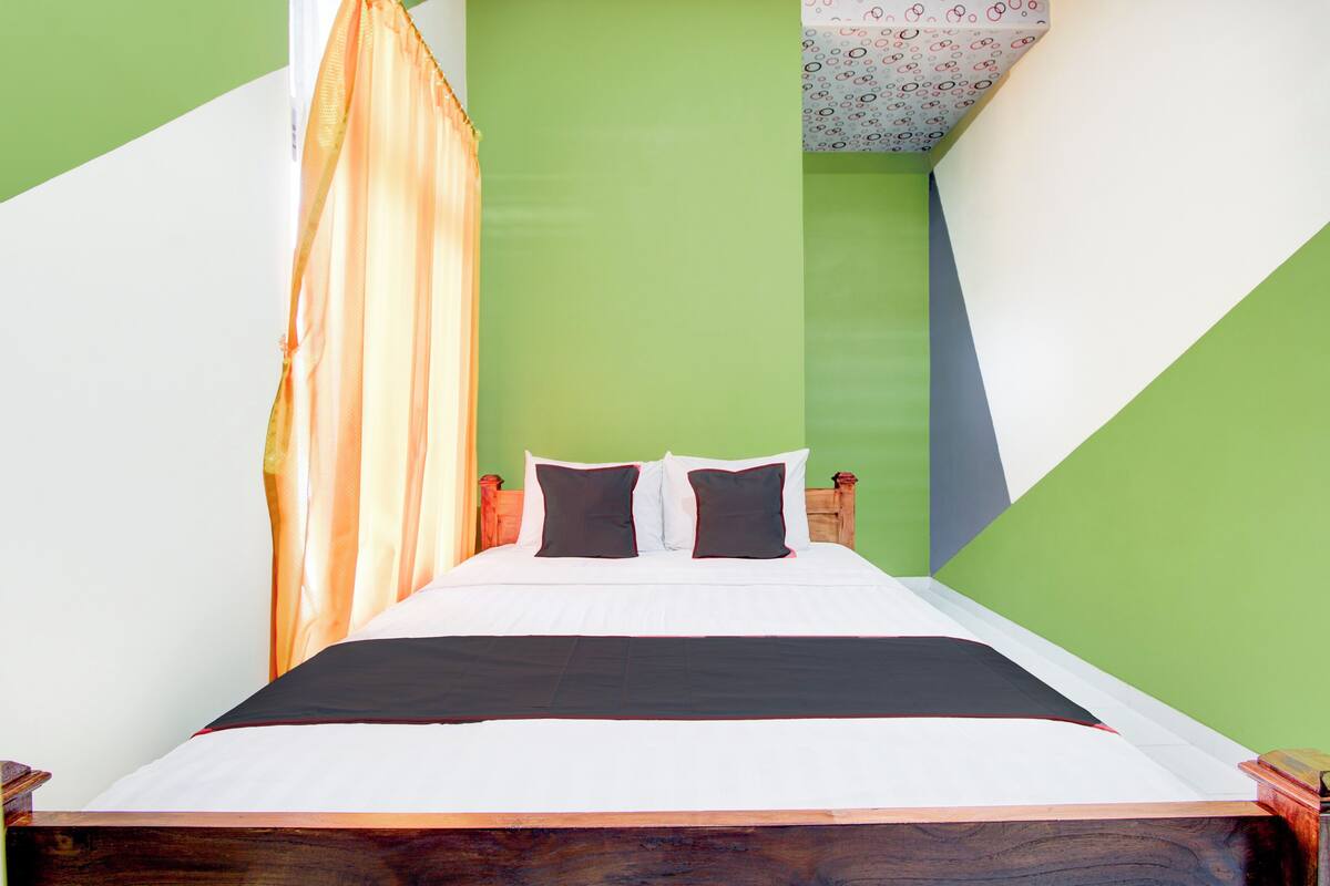 Una cama bien hecha con cabecera de madera, pared de acento verde y techo estampado.