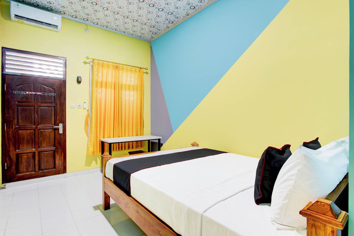 Una habitación con una cama, una puerta de madera, una ventana con cortinas amarillas y un techo con diseño circular.