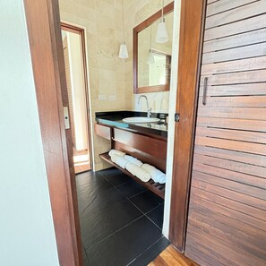 Casa de banho com toucador de madeira, lavatório e espelho. Há um porta-toalhas com toalhas e uma prateleira abaixo do toucador.