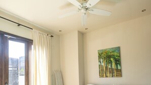 Ein Schlafzimmer mit Bett, Deckenventilator und einem Palmen-Gemälde.