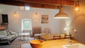 A cozy living room with a wooden dining table, a sofa, and a window. - Cozy, spacious studio / loft in charming Les Vans. Monts d'Ardèche natural park. (Les Vans)