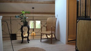 A room with a high ceiling, a skylight, a wicker chair, a small table with a potted plant, and a hanging light fixture. - Cozy, spacious studio / loft in charming Les Vans. Monts d'Ardèche natural park. (Les Vans)