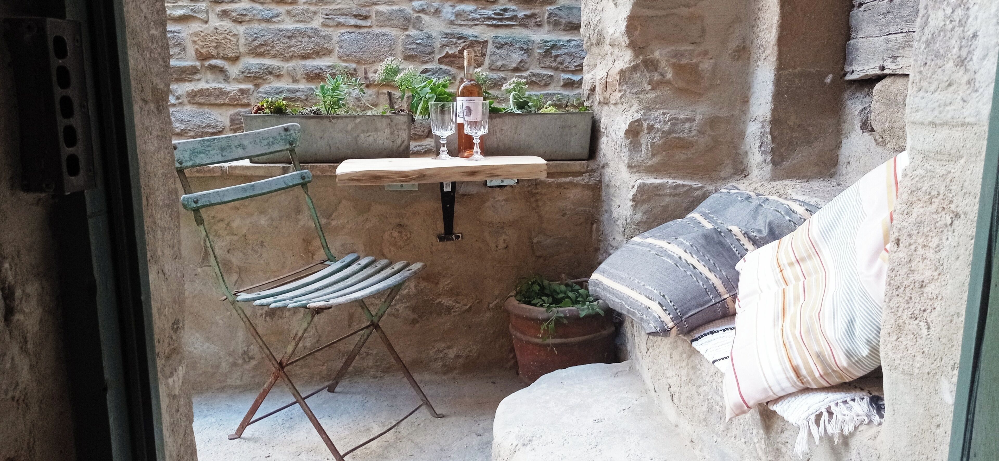 Un espace extérieur aménagé dans un style rustique, avec une table en bois, une chaise en métal et un banc rembourré.