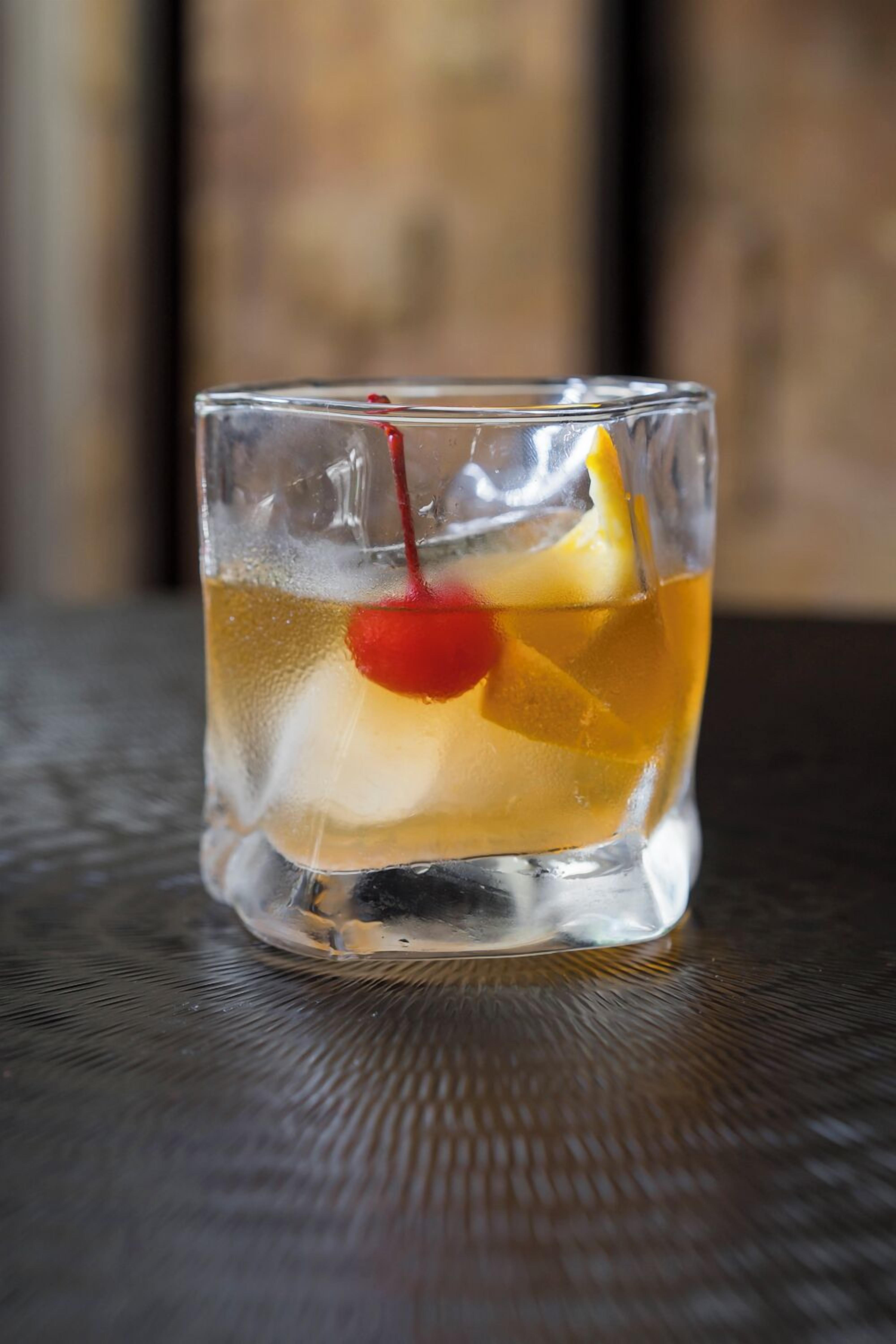 Un vaso con bebida, hielo y una cereza.