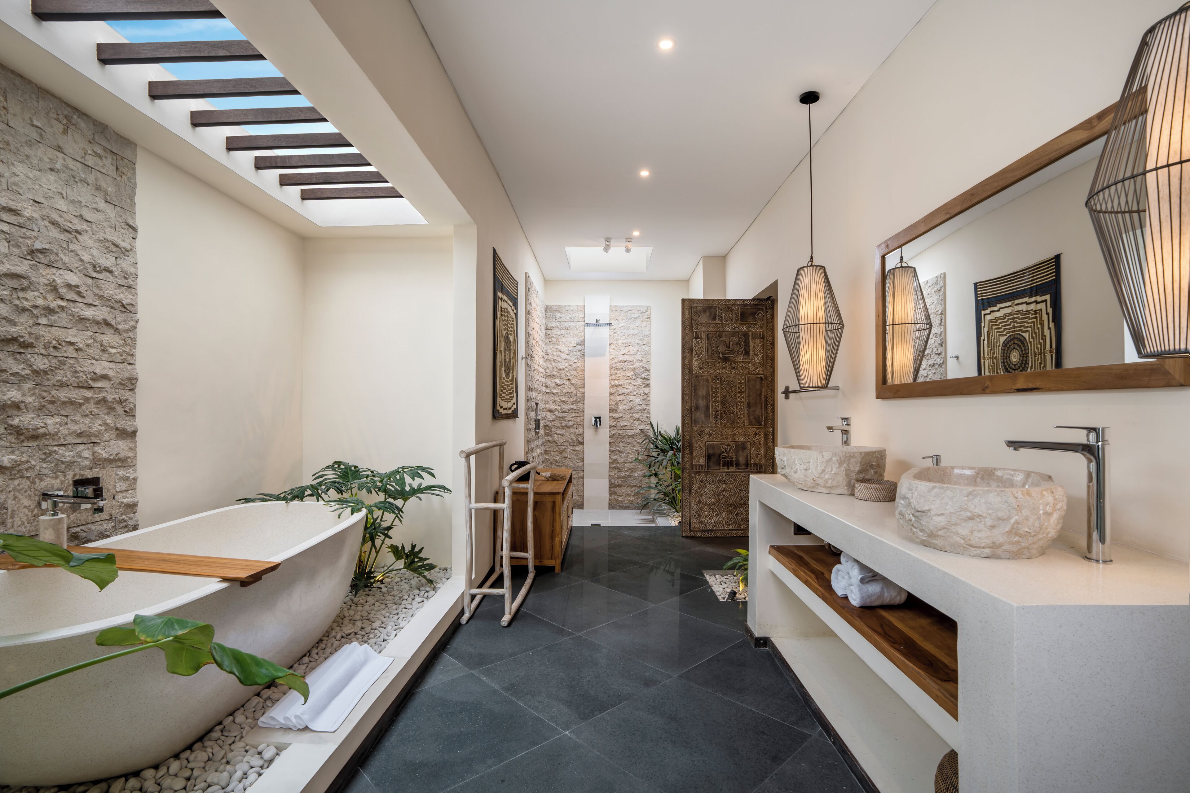 A modern bathroom with a freestanding bathtub, a vanity with a large mirror, and a skylight above the shower area.