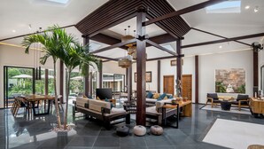 Un amplio espacio interior con techo alto, vigas de madera y una zona central de estar con sofás y una mesa de comedor.
