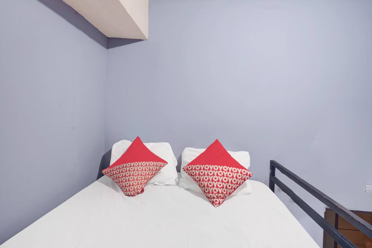A bed with white bedding and two red pillows with a repeated pattern.