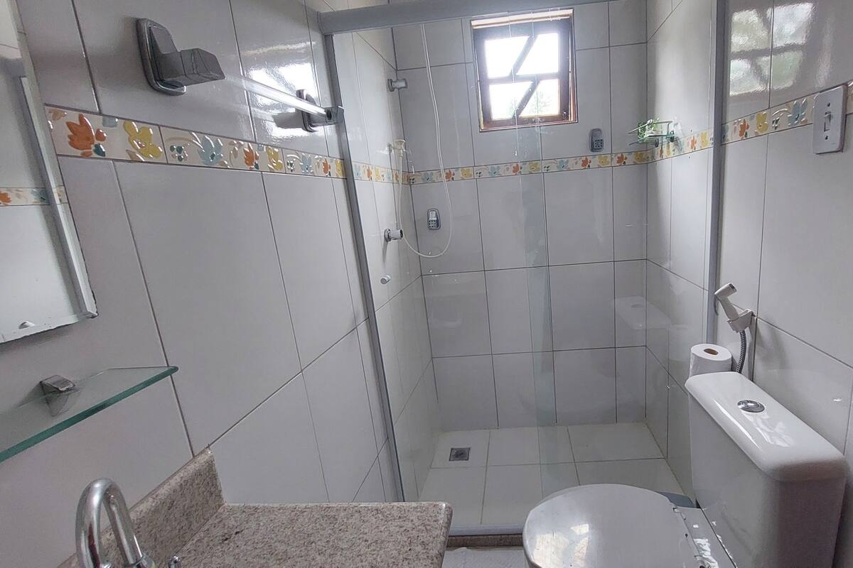 A small, tiled bathroom with a toilet, a shower, a glass shelf, and a mirror.