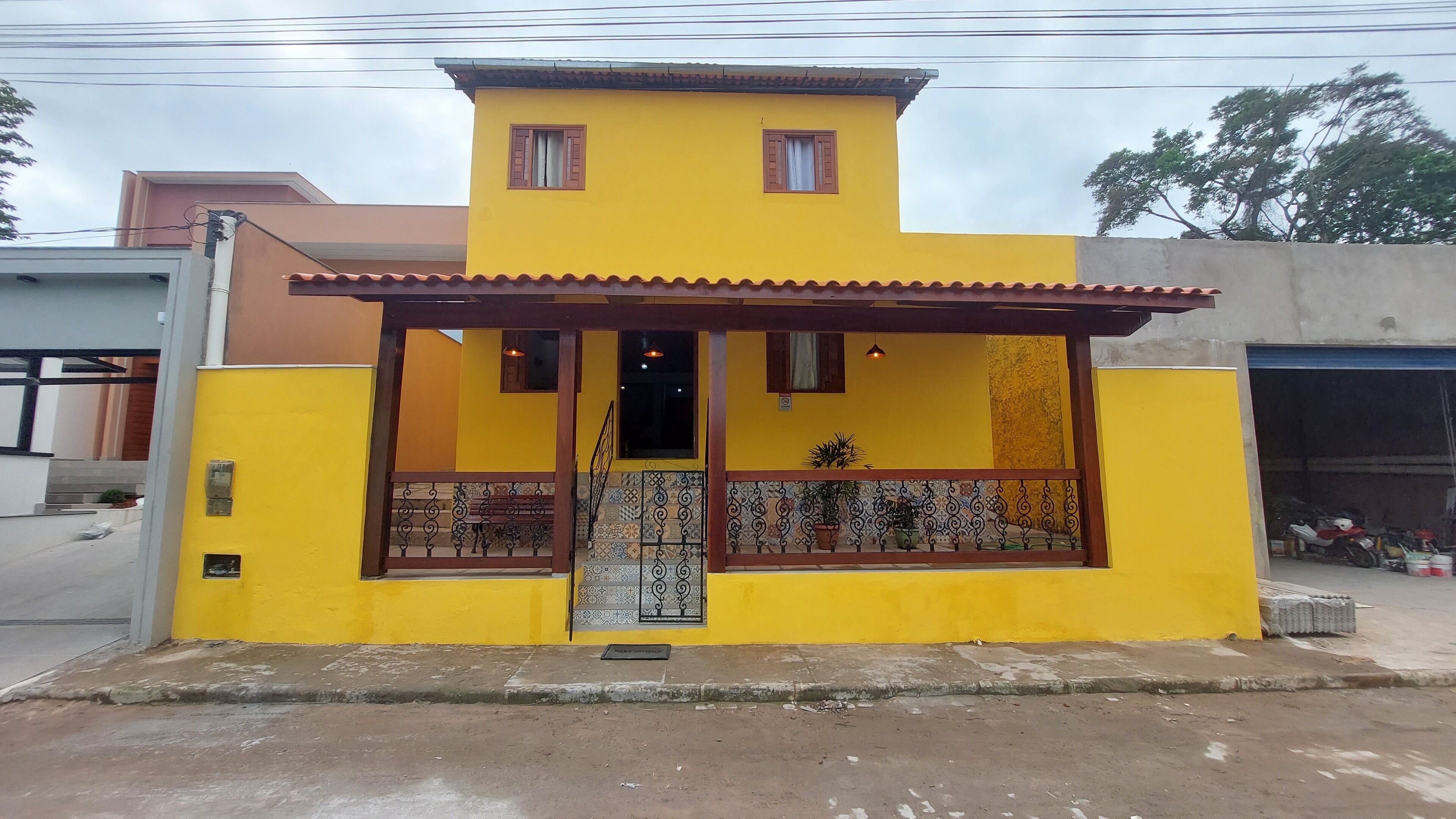 A two-story building with a yellow facade, a tiled entrance, and a balcony with a railing.