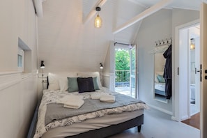 Een slaapkamer met een bed, kussens, een nachtkastje, een hanglamp en uitzicht op de omgeving.