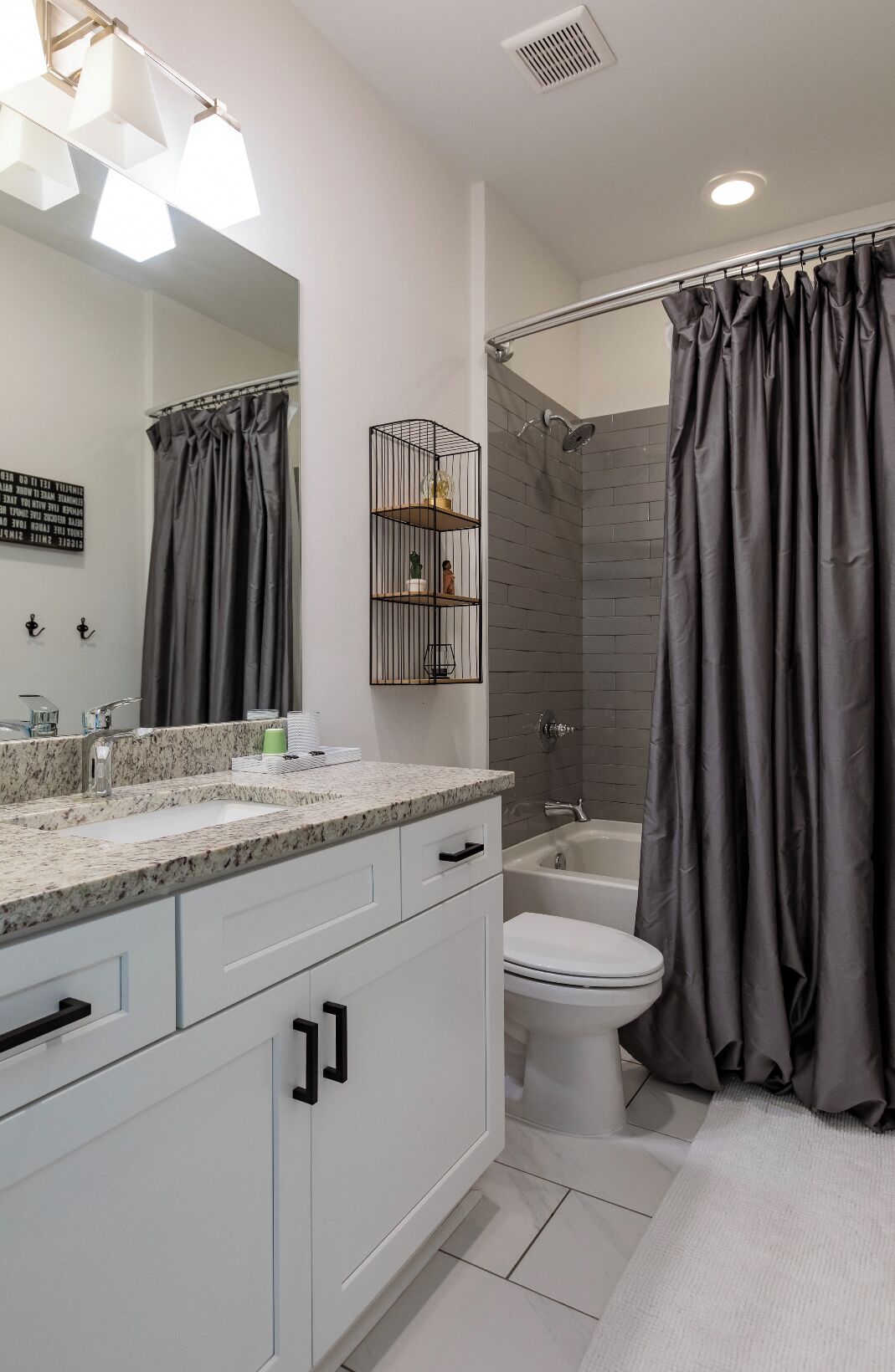 Een moderne badkamer met een wastafel met granieten blad, een toilet en een douche.