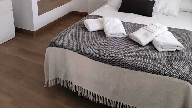 A modern bedroom with a large bed, a hanging rattan light fixture, a wooden hanger, and a small shelf. - Beautiful apartment between the Alhambra and Sierra Nevada. (Cenes de la Vega)