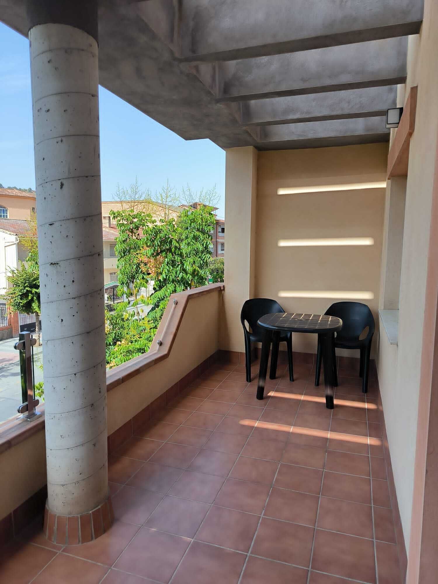 Un balcon doté d’un sol carrelé, d’une table avec des chaises et offrant une vue sur la verdure et les bâtiments.