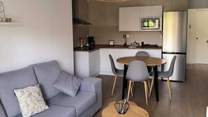 A modern living room with a grey sofa, a round wooden coffee table, and a dining area with a small round table and chairs. - Beautiful apartment between the Alhambra and Sierra Nevada. (Cenes de la Vega)