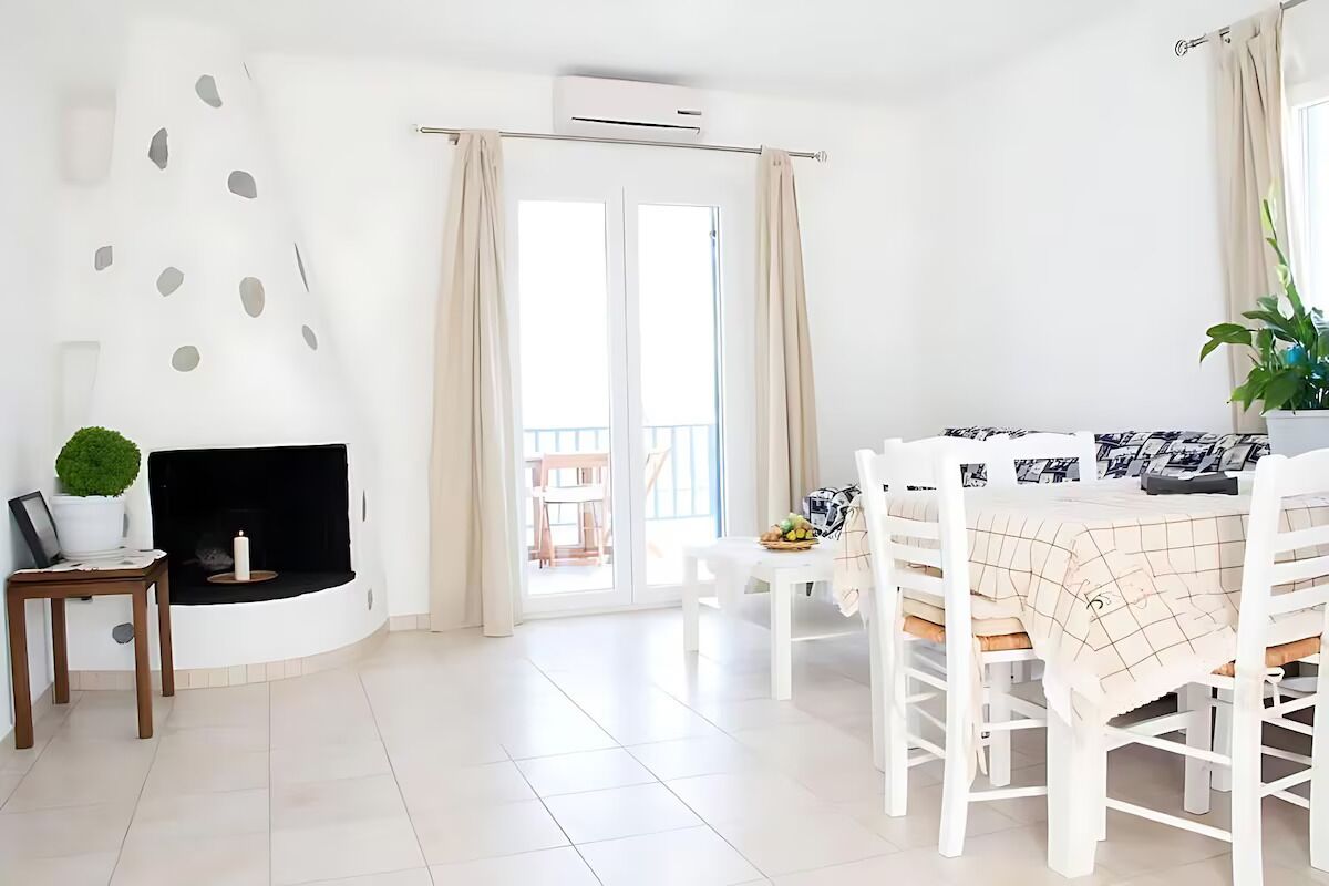 Un'ampia sala da pranzo luminosa e moderna, con un tavolo bianco imbandito per quattro persone, un tavolino laterale con una pianta e un camino.