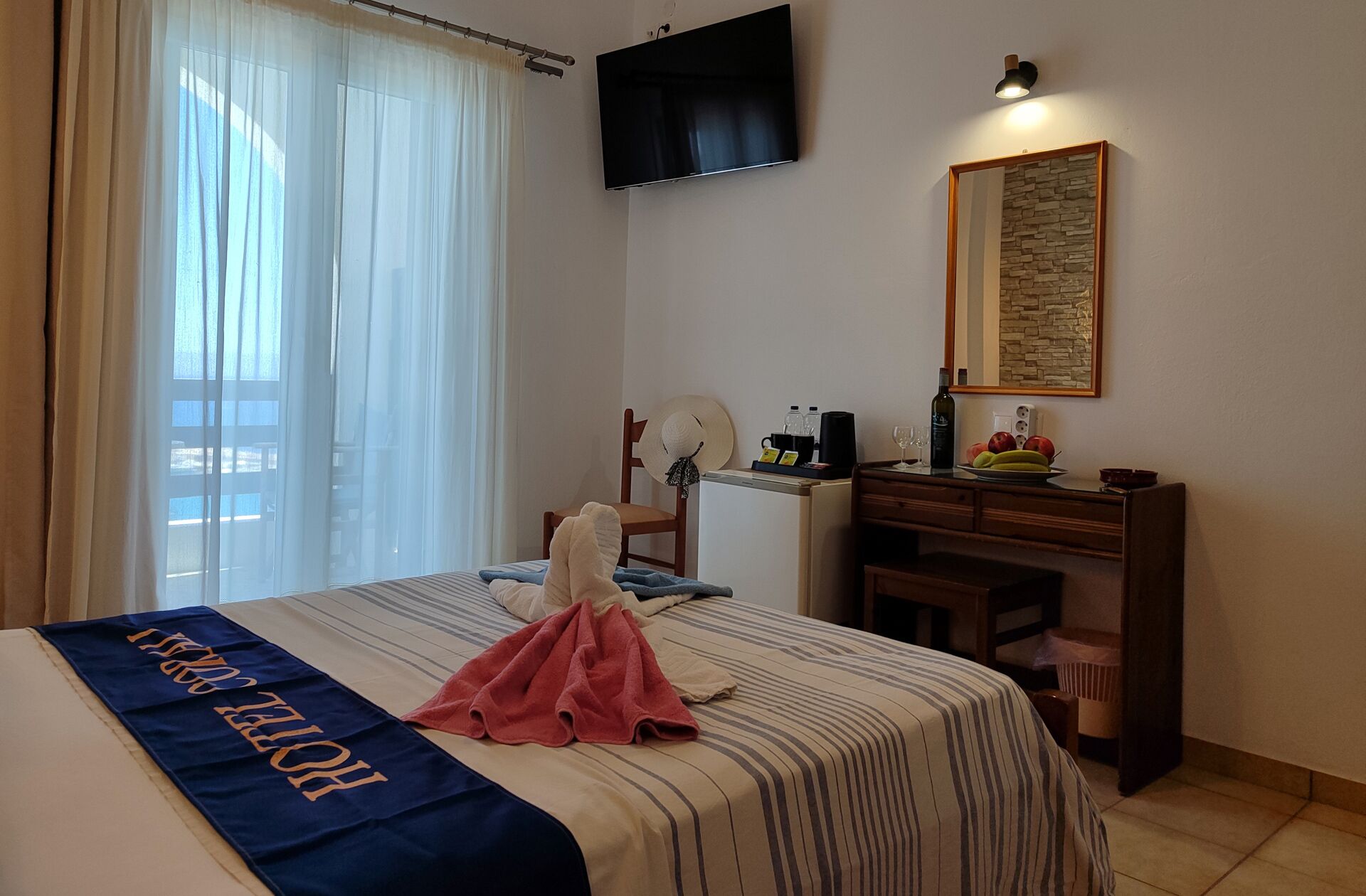 Une chambre d’hôtel équipée d’un lit, d’un bureau, d’une télévision, d’un miroir et d’une fenêtre avec des rideaux.