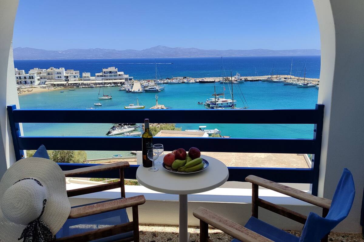 Un balcon avec une table, des chaises, une bouteille et une assiette de fruits.