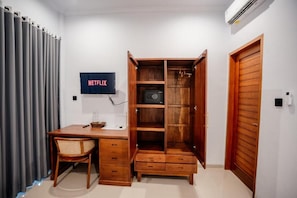 A room with a wooden desk, a chair, a wardrobe, and a wall-mounted television displaying the Netflix logo. - Pondok Yogi Guest House Canggu (Canggu)