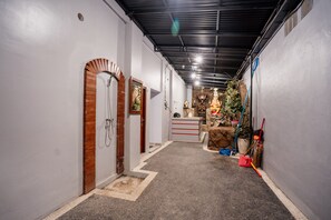 A narrow hallway with a shower area on the left, a reception desk in the center, and a statue in the background. - Pondok Yogi Guest House Canggu (Canggu)