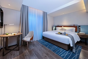 Ein modernes Hotelzimmer mit einem großen Bett, einem Schreibtisch mit Stuhl, einem Fernseher und einem Fenster mit Vorhängen.