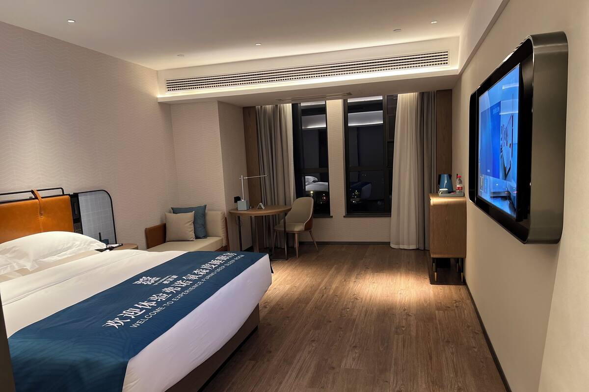A hotel room with a bed, a desk, a chair, a TV, and a view of the city at night.