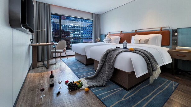 Een hotelkamer met een groot bed, een bureau, een stoel, een televisie en uitzicht over de stad.