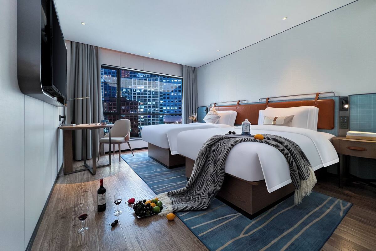 A hotel room with a large bed, a desk, a chair, a TV, and a city view.