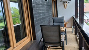 A wooden deck with a table and chairs, a mounted deer head, and a window overlooking greenery. - Apartment 55 sqm for 2 persons with balcony and mountain view (Anger)