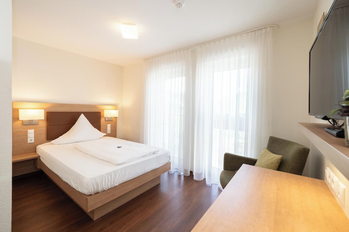 Een hotelkamer met een bed, nachtlampjes, een houten tafel, een stoel en een televisie aan de muur.