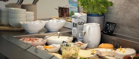 A buffet setup with various food items, including bowls of soup, cheese, and meat.