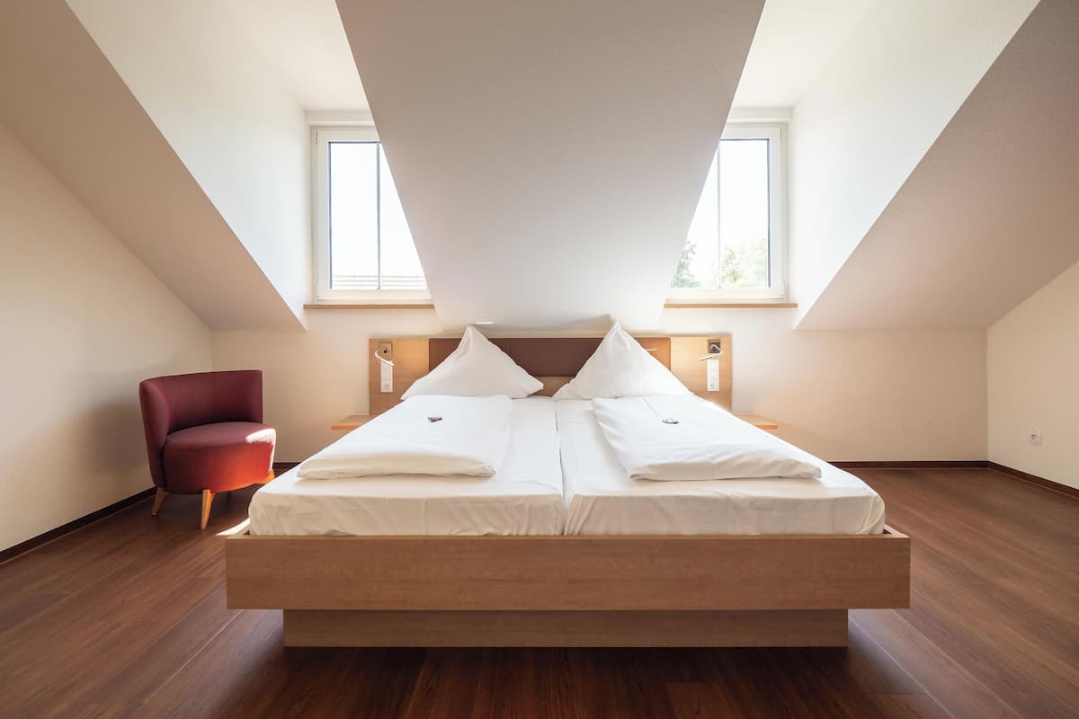 Een slaapkamer met een groot bed, twee nachtkastjes, een rode stoel en twee ramen.