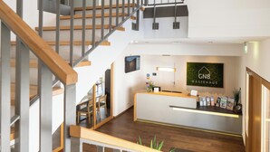 A reception area with a modern design, including a wooden staircase, a reception desk, and a sign for Gastehaus.