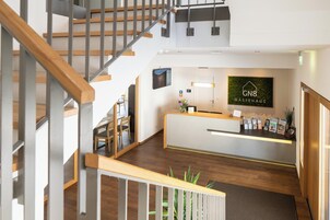 Un área de recepción con diseño moderno, que incluye una escalera de madera, un mostrador de recepción y un cartel de Gastehaus.