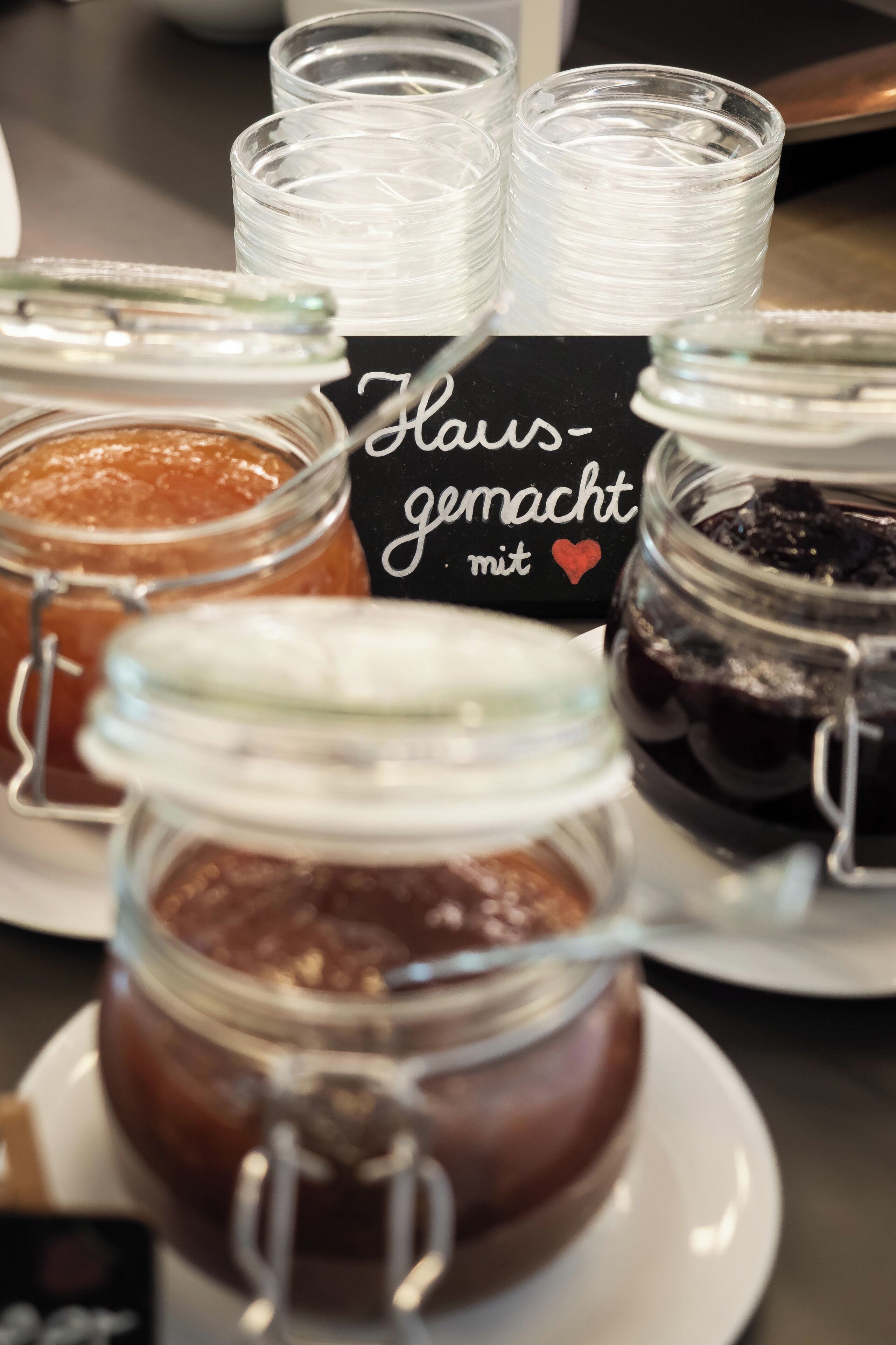Une table avec différentes sortes de confitures en pots et une pancarte sur laquelle on peut lire : « Fait maison avec amour ».