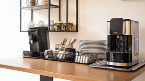 A coffee station with a coffee maker, a water dispenser, and a tray with cups and utensils.